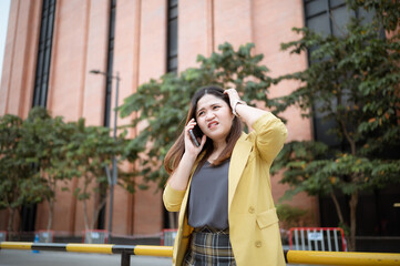 Young Asian woman using her phone to chat and send messages outdoors , Talking on the phone, headache with customers .Concept of business and communication