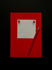 Red notebook with white blank sticker, red pen on black background. Flat lay, top view. 