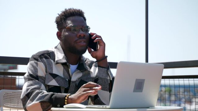 young black man is working with laptop computer in cafe and calling by mobile phone, portrait