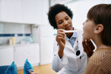 African American pediatrician examining throat of small boy at doctor's office.