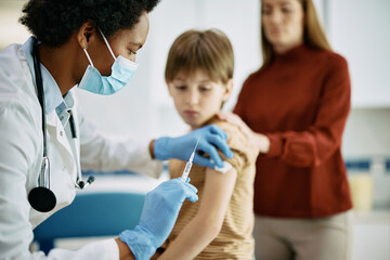 Black female doctor vaccinating small boy at medical clinic.