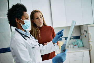 Mid adult woman and black female doctor examining X-ray image at medical clinic.