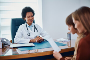 Obraz premium Black female pediatrician having medical appointment with mother and child at clinic.