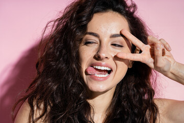 Fototapeta premium Young woman with freckles showing peace sign on pink background.