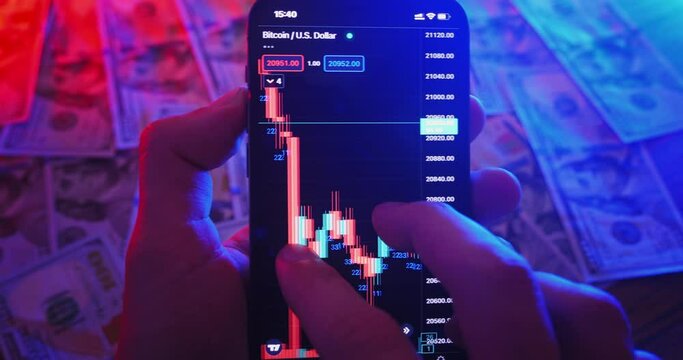 Cryptocurrency earning concept. Mobile trading cryptocurrency market analysis. Close-up person pro trader using mobile phone app analyzes crypto market, investing in crypto, money on table background