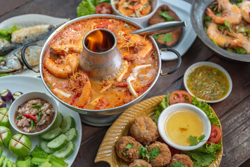Tom Yam Kung or Tom Yum soup is Thai hot spicy soup shrimp or prawn with lemon grass, lemon, galangal, mushrooms, coconut milk and chili in bowl on wooden table top view, famous Thai food cuisine.