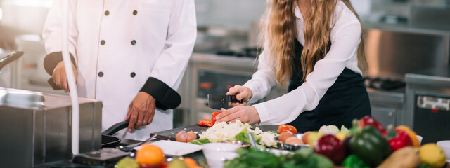 Caucasian schoolgirl holding vegetable basket in cooking classroom, Senior chef teaching to select...