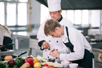 Mature asian teacher teaching schoolboy chef students to select ingredient for cooking in class.