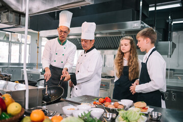 Group of diverse student chef learning cooking class in the kitchen. Mature asian teacher teaching diverse chef students at school.