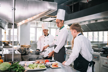 Group of diverse student chef learning cooking class in the kitchen. Mature asian teacher teaching diverse chef students at school.