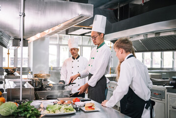 Group of diverse student chef learning cooking class in the kitchen. Mature asian teacher teaching diverse chef students at school.