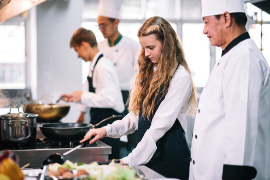 Group of diverse student chef learning cooking class in the kitchen. Mature asian teacher teaching diverse chef students at school.