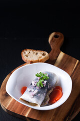 Food concept roll Pickled Herring in white bowl on black background with copy space