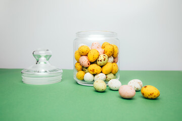 Chocolate colorful decorative eggs in a glass jar on a white-green background. Happy Easter. Front view