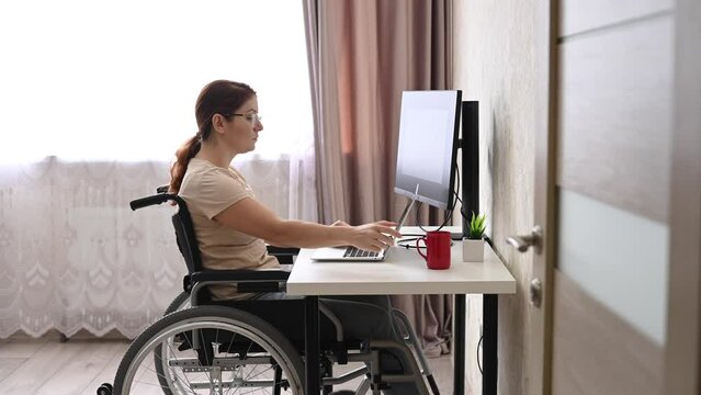 Caucasian woman with disabilities working at the computer while sitting in a wheelchair. 