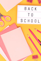 Back to school. Lightbox with letters and pink colored stationery on a yellow background.