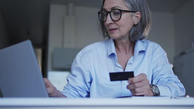 Senior woman entering credit card number on laptop, registers in banking app