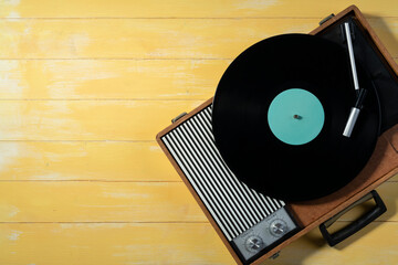 Old gramophone with a vinyl record on yellow wooden table, top view, vintage style.