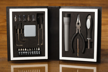 mini caja de herramientas, destornilladores, linterna y wincha de medición en fondo texturizado de madera.