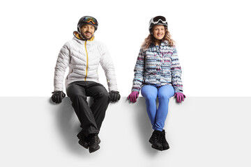 Young man and woman wearing winter jackets and helmets and sitting on a blank panel