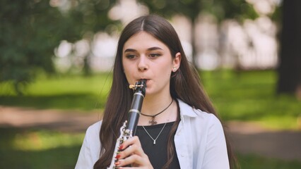A girl plays the clarinet in the park. - obrazy, fototapety, plakaty