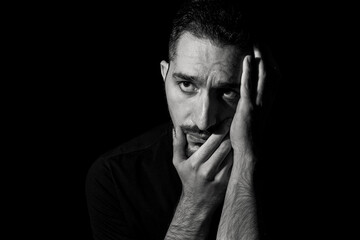 Black-white male portrait on a black background. A sad man clutches his face with his hand