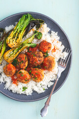 Bowl of chicken meatballs in sweet chili sauce with rice and baby Pak choi or Bok choy (Chinese cabbage),  green spring mint background. Hong Kong fusion cuisine inspired by street food