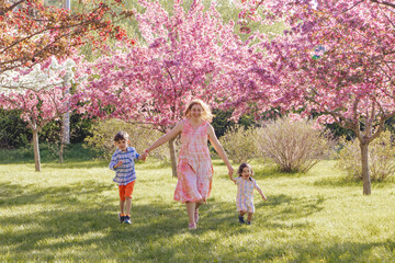 Obraz premium Woman holding hands with children while wallking happily at a park in Spring
