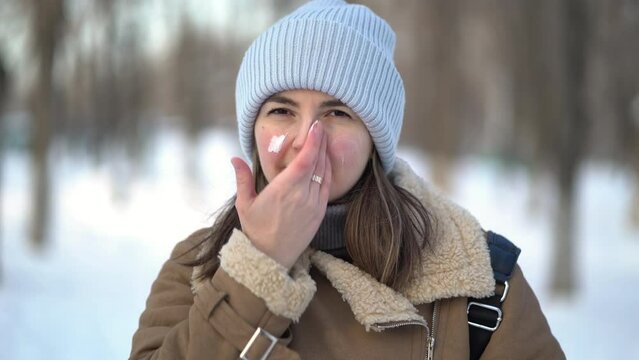 Portrait of a woman applying facial moisturizer cream in winter.