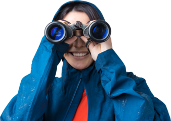 A tourist girl in a blue raincoat holds binoculars in her hands and looks into the distance, spies.
