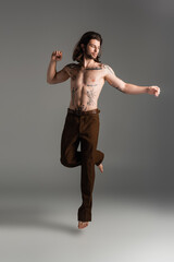 Shirtless and tattooed man jumping on grey background.