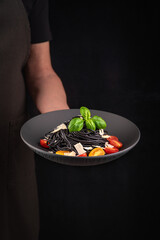 The Chef Holds a Platte of Spaghetti with tomatoes ,basil and parmesan.
