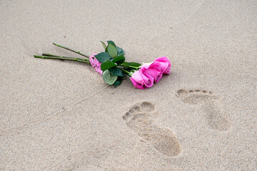 Pair of footprints in beach sand with pink roses and a ruffled ribbon