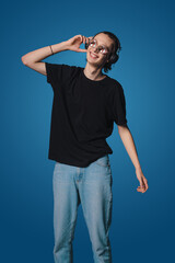 Naklejka premium Young caucasian musician wearing sunglasses in headphones listening to music isolated over blue background. Concept of music, hobby, festival.