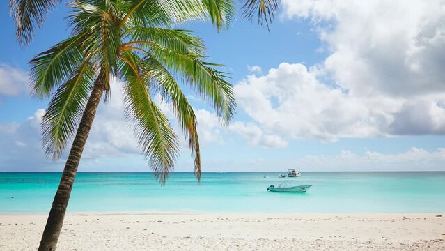 Beautiful beach landscape with palm trees on white sand and a boat against a blue sky with clouds. Paradise island on a sunny summer day. Romantic idealistic image of an exotic beach holiday.