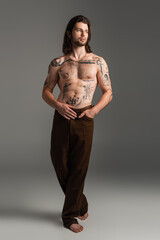 Full length of tattooed and shirtless man with tattoo on body on grey background.
