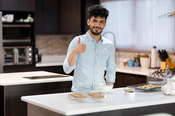 Fototapeta na wymiar Young Hispanic man baking homemade cookies - Young man preparing cookies - Young man giving thumb up in kitchen
