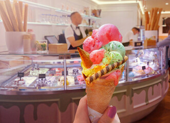 Italian ice - cream cone held in hand on the background of  shop  in Rome , Italy .It is one of the best ice cream place in town popular among tourists - 567121430