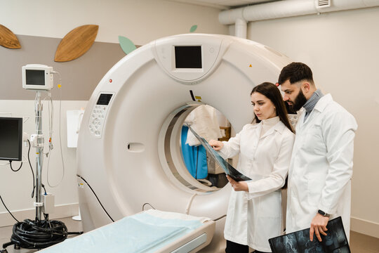 CT Computed tomography scan procedure to obtain detailed internal images of body and research on tumors in head, brain, and spine. Colleagues doctors discussing x-rays after CT scan of abdomen.