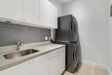 Laundry room with quarts counter top, sink, stacked washer and dryer.