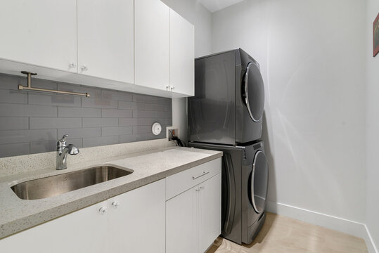 Laundry Room With Quarts Counter Top, Sink, Stacked Washer And Dryer.