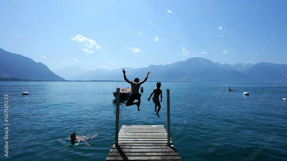 Wall mural people jumping into lake water. father and son running in swiss pier and diving into geneva lake lan