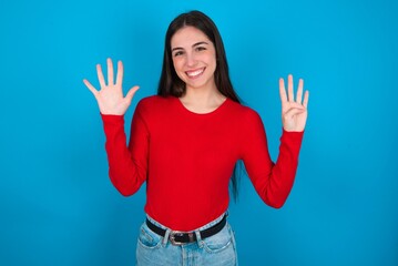 young brunette girl wearing red T-shirt against blue wall showing and pointing up with fingers...