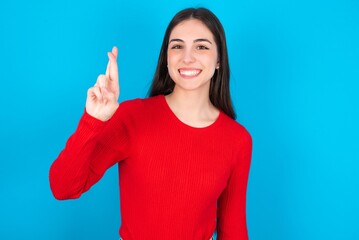 young brunette girl wearing red T-shirt against blue wall pointing up with fingers number ten in Chinese sign language Shi