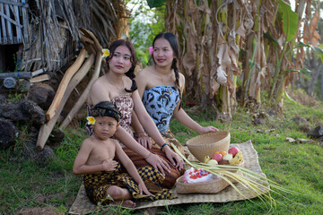 Balinese family of sisters and brothers sit on a reed and bamboo mat preparing offerings. Bamboo...