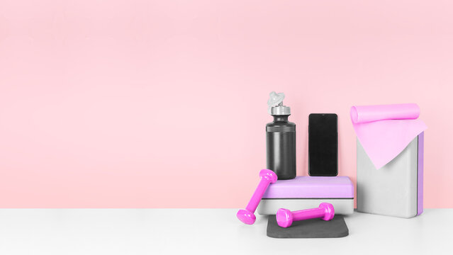 Fitness equipment and smartphone on a pink background, front view, copy space. Smart fitness training.