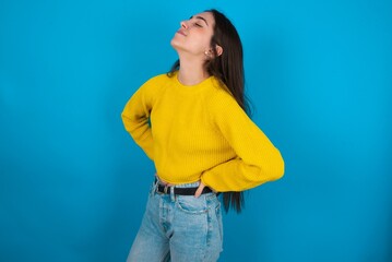 young brunette girl wearing yellow knitted sweater against blue wall got back pain
