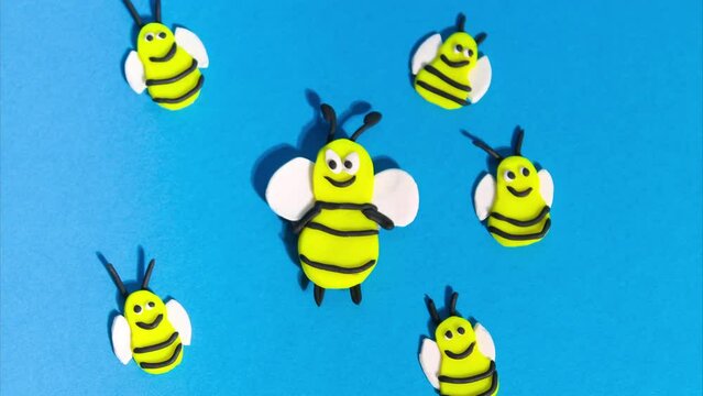 Stop motion animation from plasticine. Cheerful funny bees flying on a blue background. Claymotion cartoon