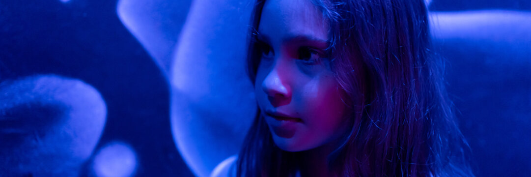 Portrait Face Cute Happy Candid Caucasian Preteen Nine Year Old Kid Girl In Profile In The Studio Illuminated By Blue Purple Neon Light. Banner