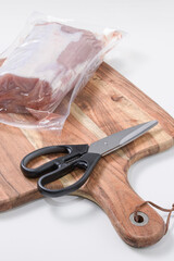 Scissors for removing vacuum plastic. A piece of meat in plastic vacuum packaging and kitchen...